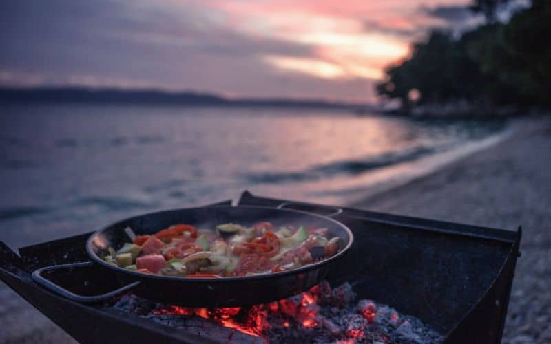 Vegetables frying in a pan over coals at the seaside