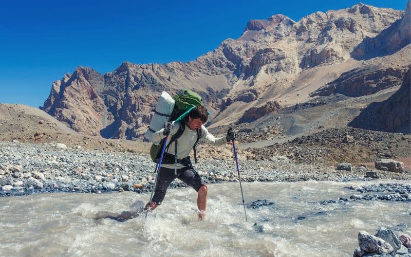 Hiker wading across a river holding walking poles