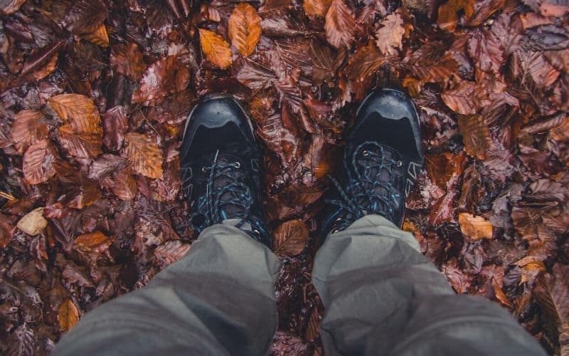 Man weating hiking boots and wet trousers standing in a pile of wet leaves