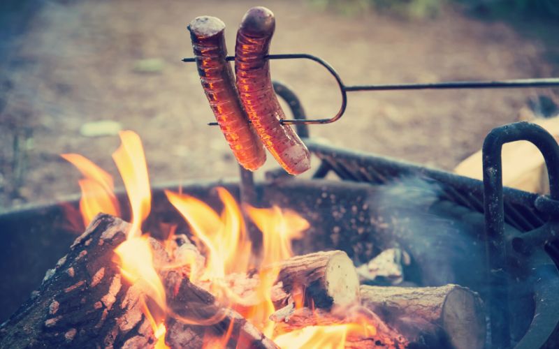 Cooking sausages on a long fork over a campfire