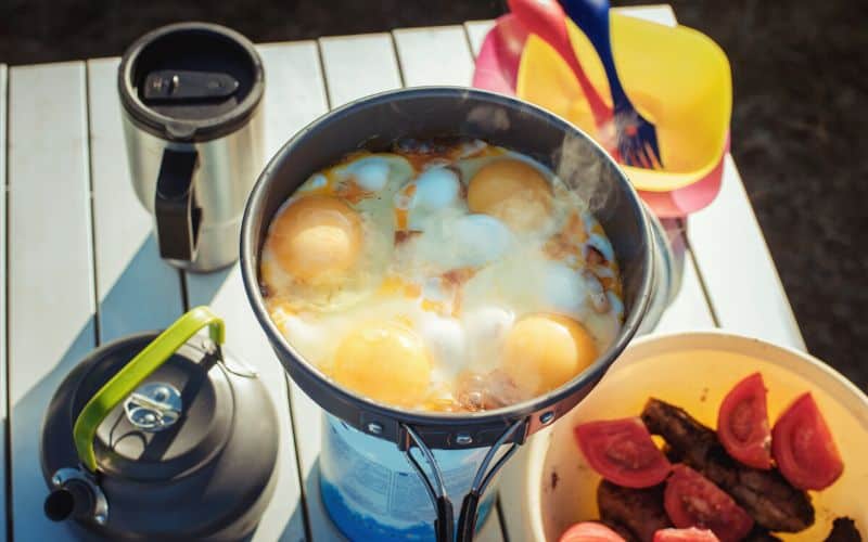 Eggs cooking on camping stove sitting atop an aluminum camping table
