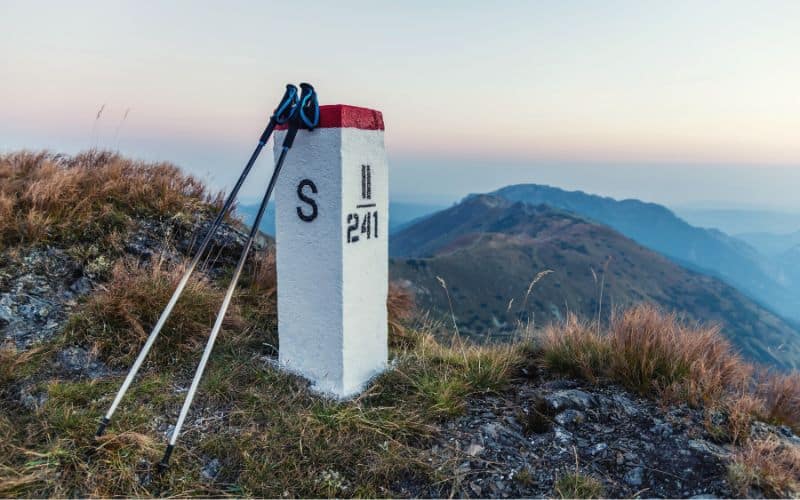 Extended trekking poles leaning against trail marker