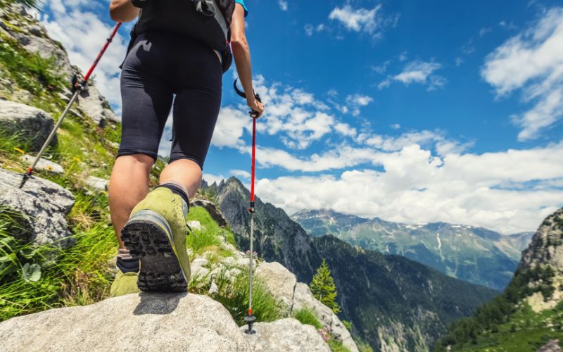 Hiker with trekking poles hiking in mountains on sunny day
