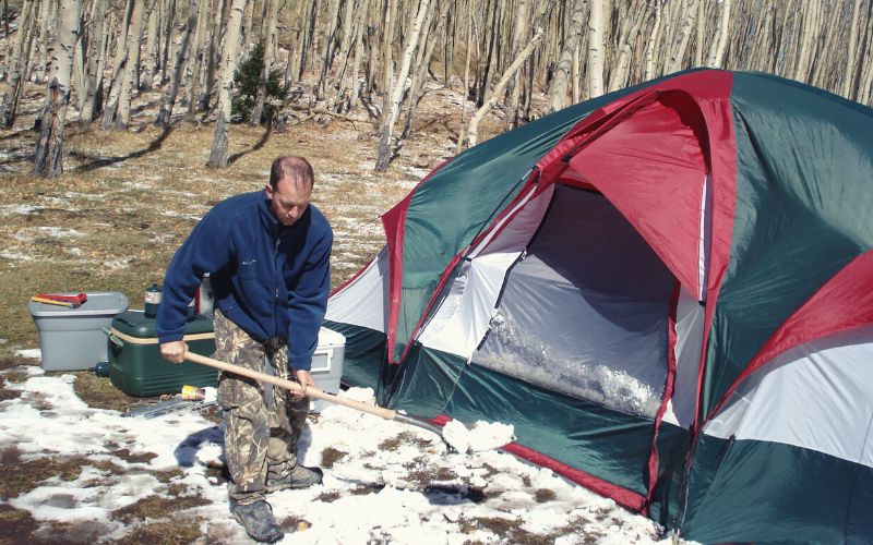 Man clearing snow in front of tent with a long handles shovel