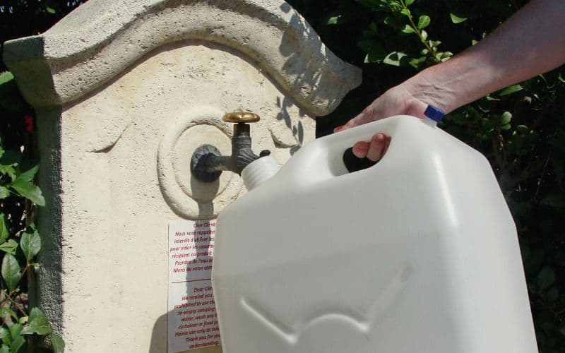 Person filling up water container at campsite tap