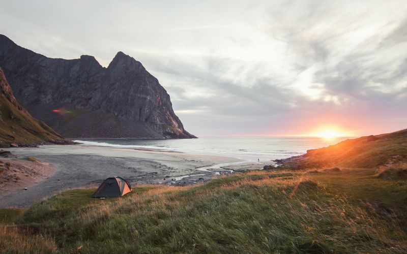 Tent pitched on beach with sun rising over horizon