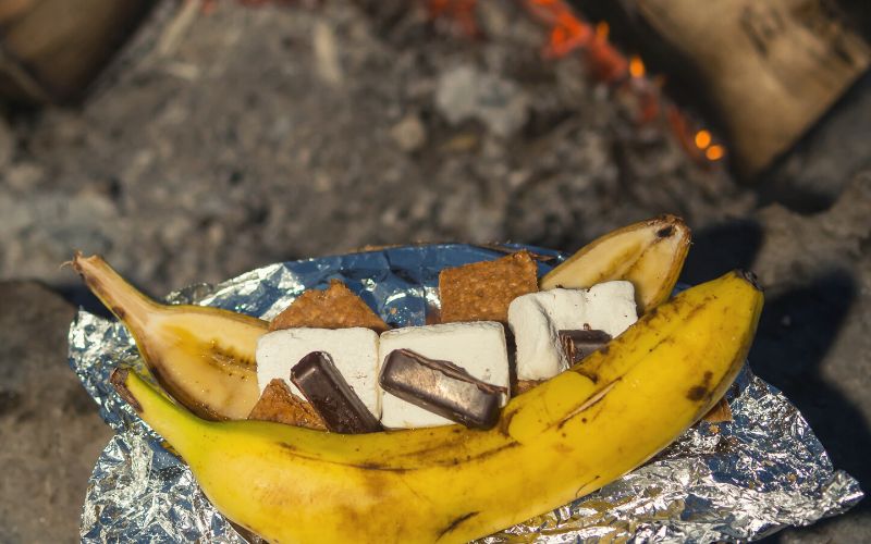 Banana in foil filled with marshmallow and chocolate in front of a campfire
