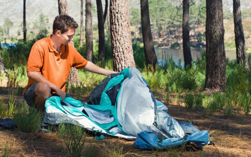 man pitching tent in forest