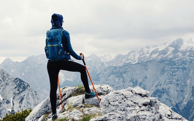 Hiker with trekking poles standing on top of mountain wearing leggings