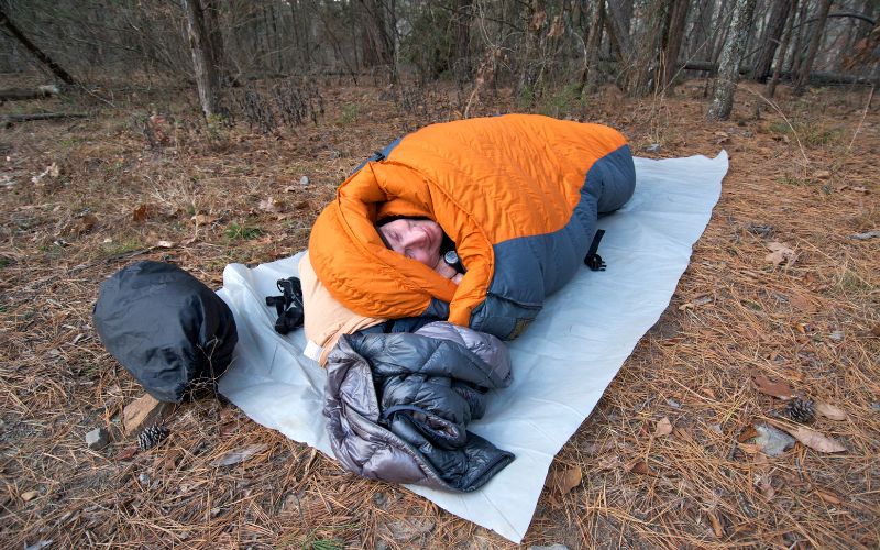 Man in sleeping bag on top of a tarp 