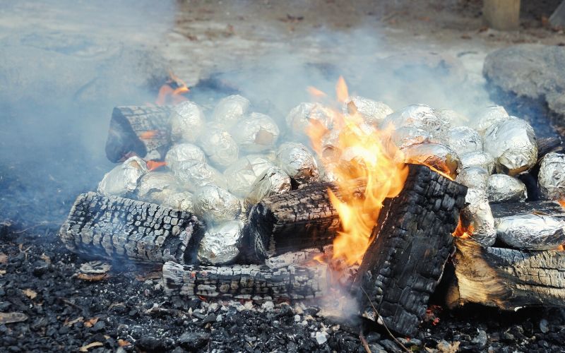 Many potatoes wrapped in foil inside a campfire