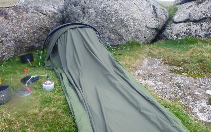 Olive green bivy bag pitched behind some rocks