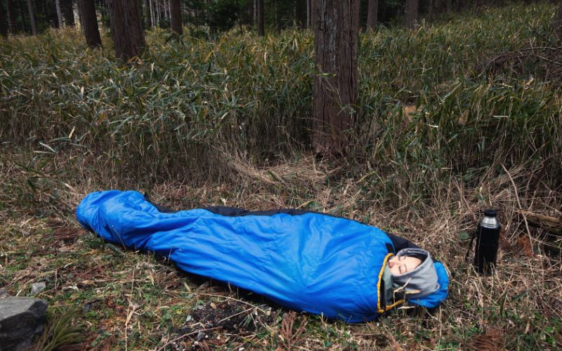 Woman sleeping in sleeping bag on thick grass