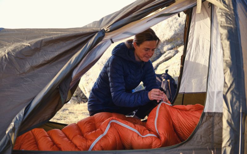 Woman zipping up a sleeping bag in a tent