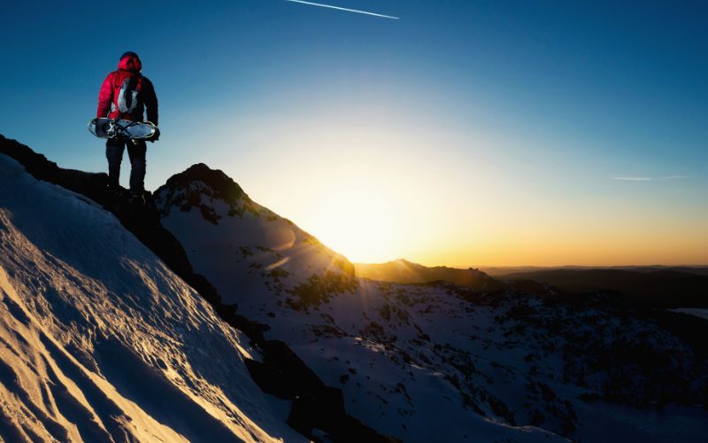 Hiker standing on top of mountain looking at a sunset