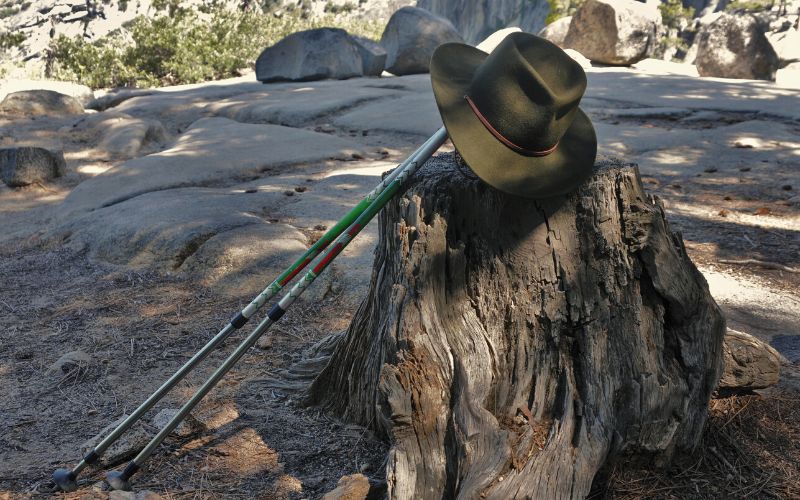 A sun hat for hiking propped up on trekking poles against a tree stump