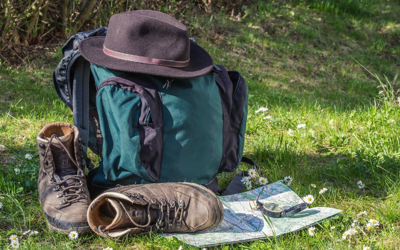 Backpack, boots, hat, map and compass lying on grass