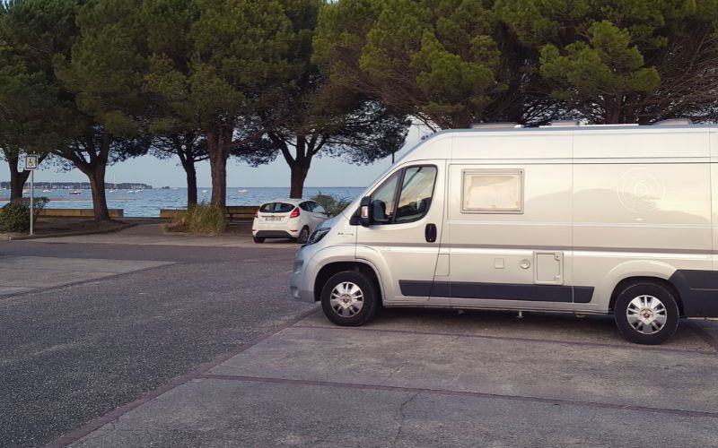 Camper van parked in car park beside a scenic lake