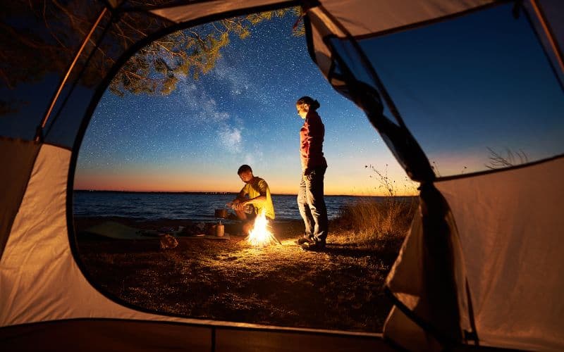 View from inside tent of 2 campers around a campfire