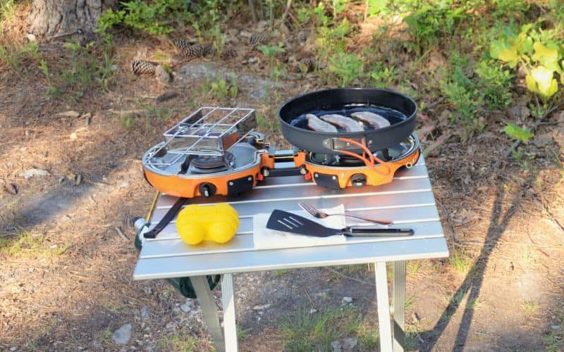 Camping stove with two burners cooking bacon