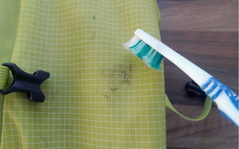 Cleaning muddy stain on backpack with toothbrush