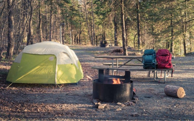 Empty campground with one tent pitched and fire burning