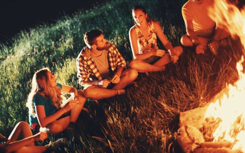 Group of adults sitting in a large circle around a campfire playing 'Would you rather?'