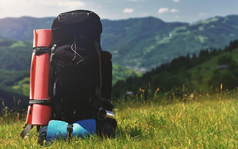 Packed hiking backpack sitting in field in front of mountains