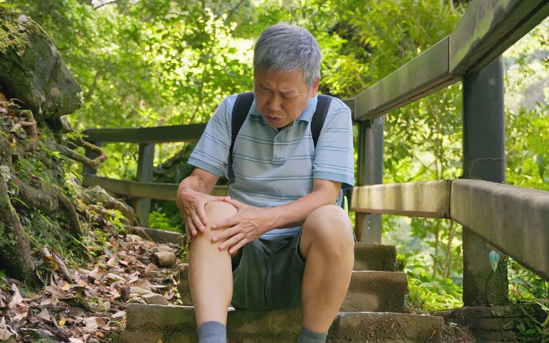 Man sitting on step on a forest trail holding his knee