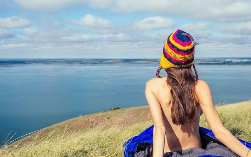 Naked hiker sitting with sleeping bag wrapped round her