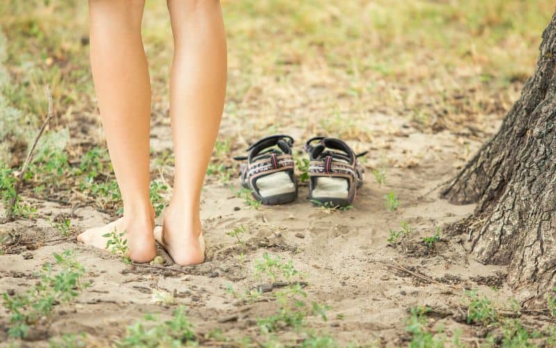 Naked hiker taking sandals off to feel feet on the ground