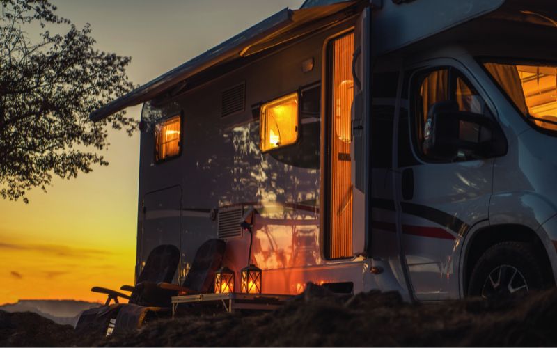 RV at dusk with lights on and camp chairs outside