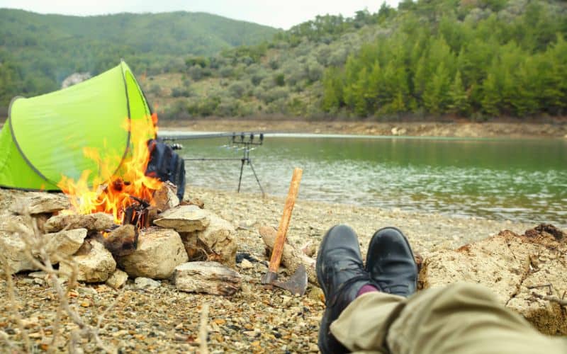 Small campfire in fire pit beside a tent and a river