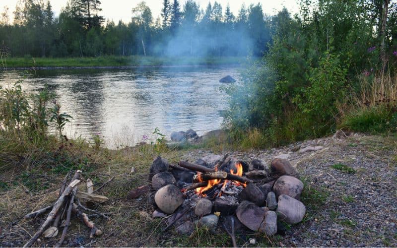 Small lit fire in fire pit beside a river