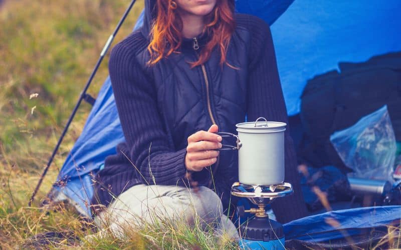 Woman heating water on a camp stove in front of her tent
