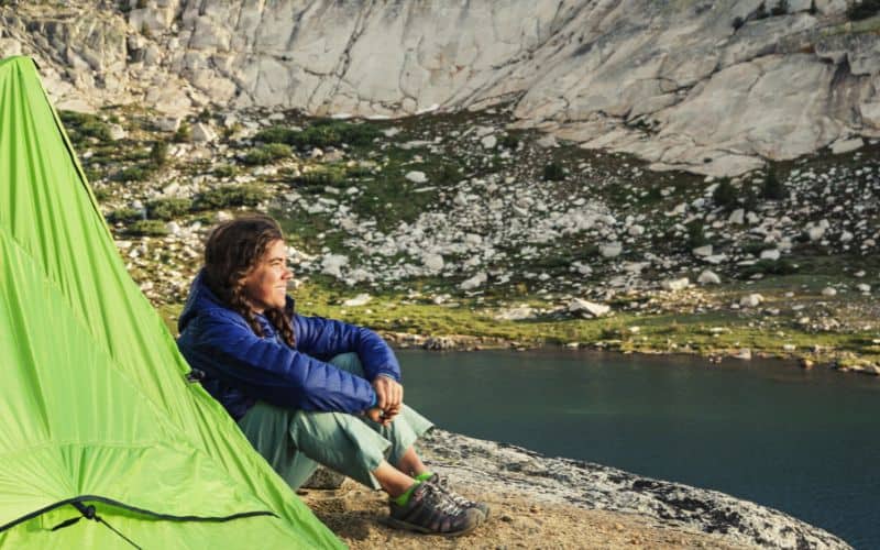 Woman sitting in front of tent and lake