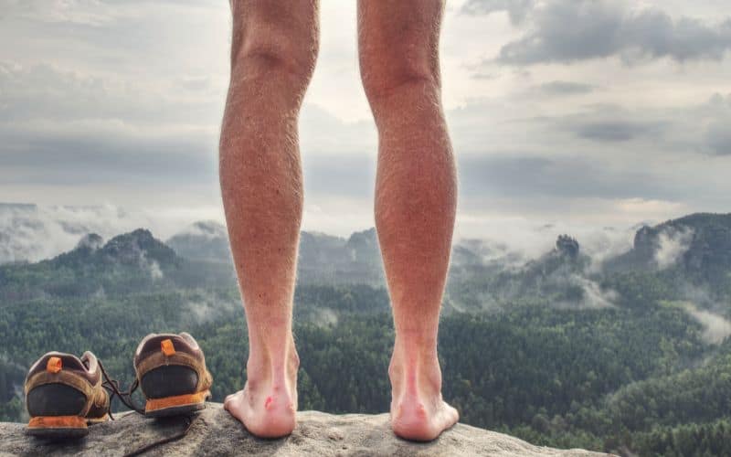 Naked hiker with sandals beside him standing on top mountain