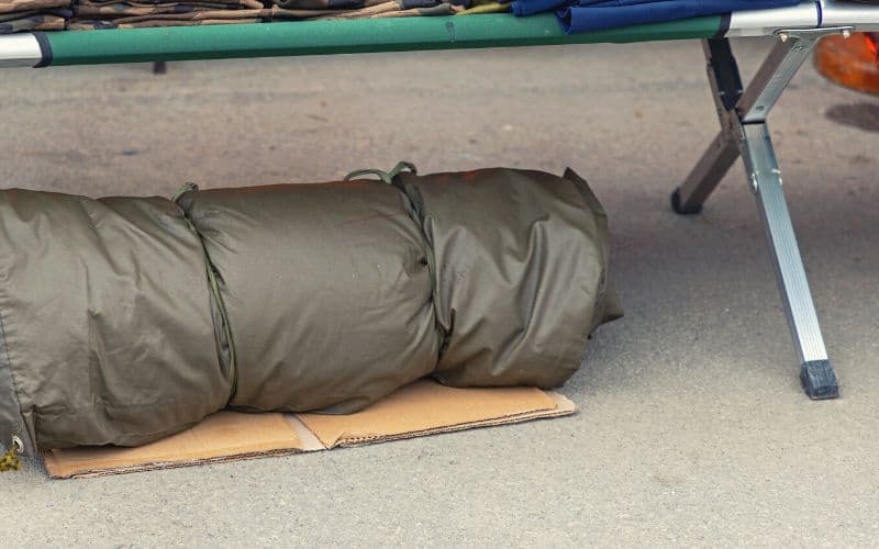 A metal framed cot bed with tarp rolled up underneath it