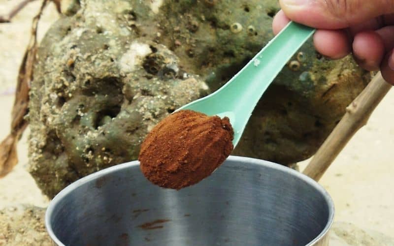 Adding coffee to metal tin at the beach