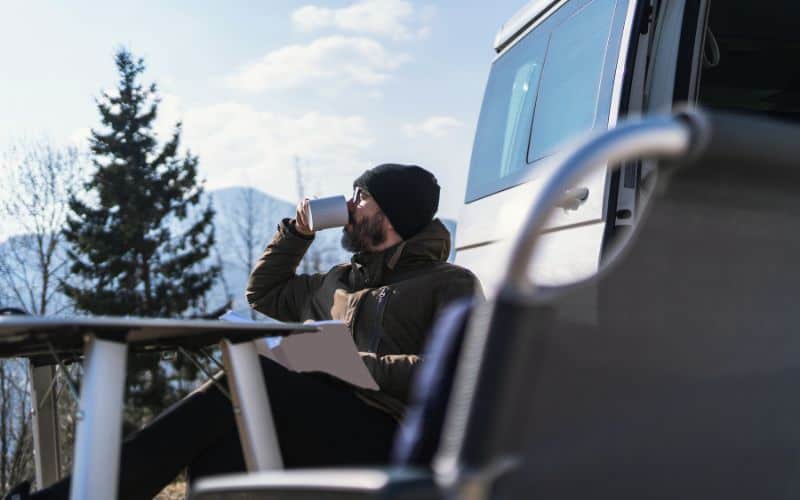 Camper sitting outside of RV drinking coffee from a mug 