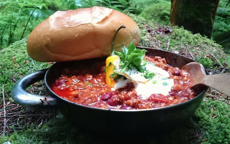 Skillet of chili with a bread roll sitting on a mossy mound
