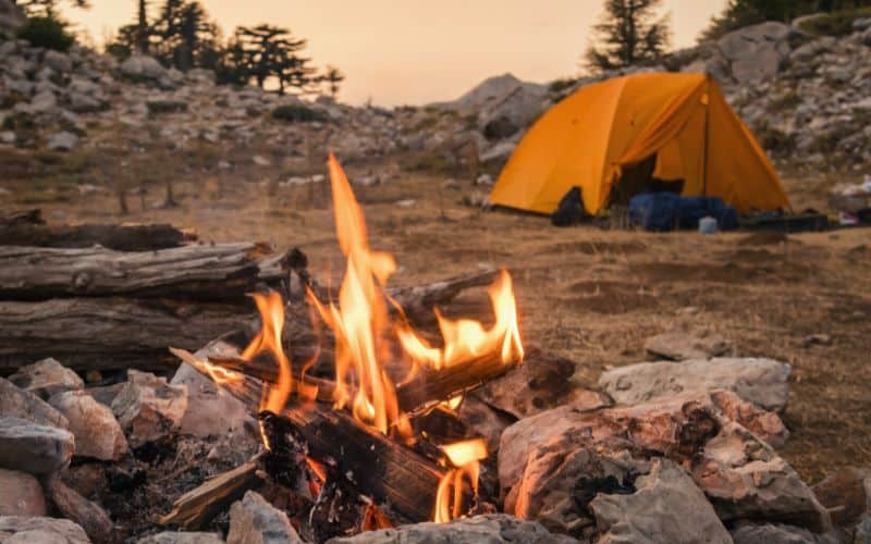 Campfire burning with a tent pitched in the background