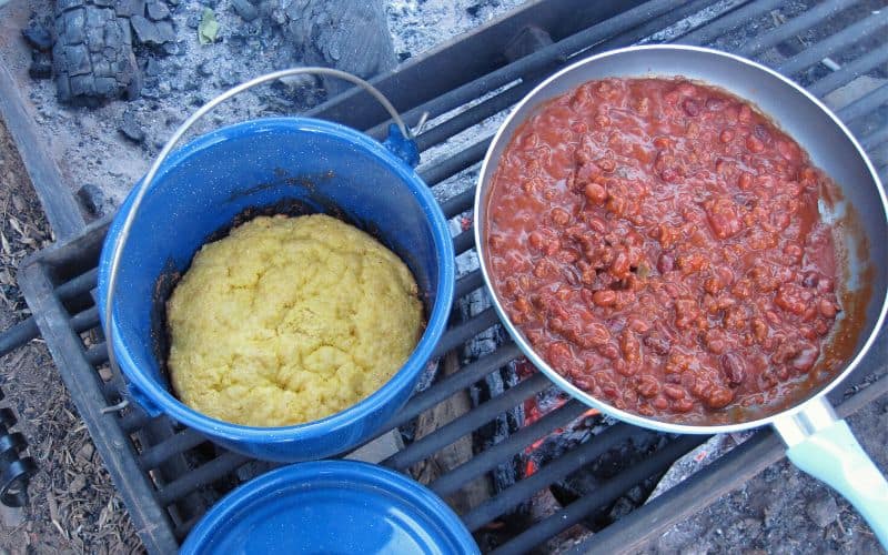 Campfire chili and cornbread cooking over a grill over a fire 