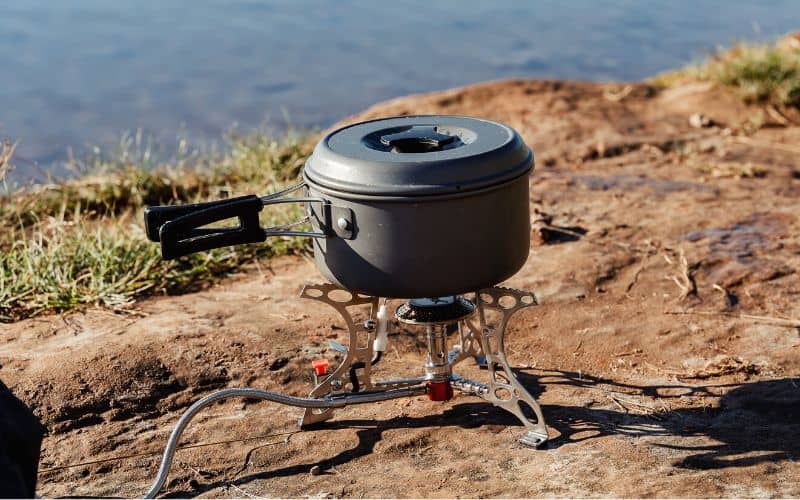 Camping stove with fuel line with pot on top in front of an ocean view
