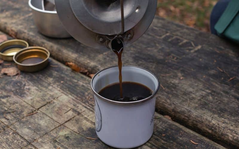 Coffee being poured from a camping coffee pot into metal mug