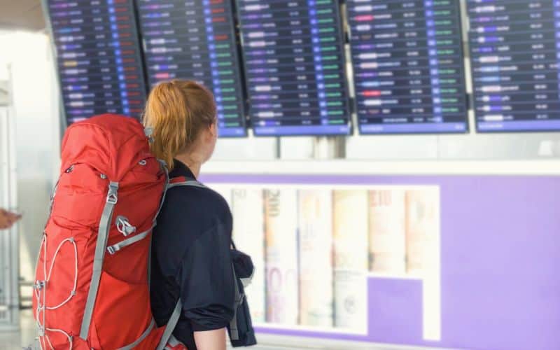 Hiker with large backpack on looking at flight departure board