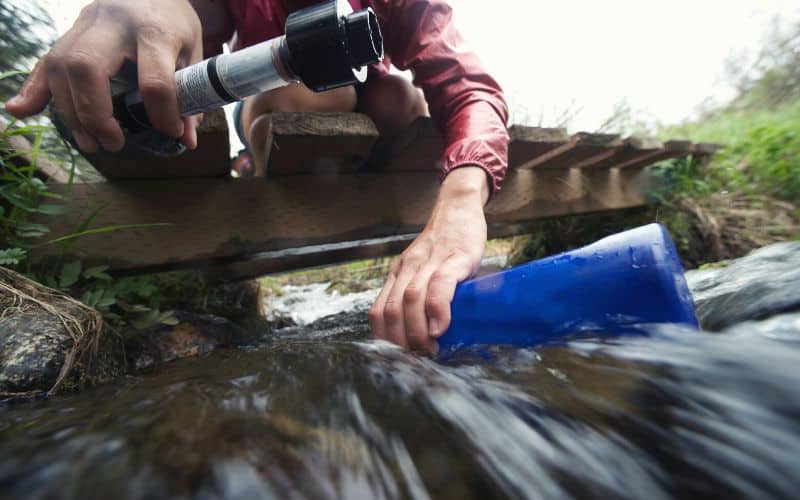 Hiker filling water bottle from stream while holding a water filtration device