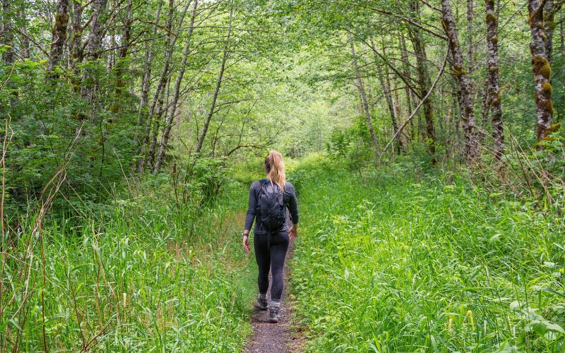 Hiker in leggings walking through tall grass in a wooded area