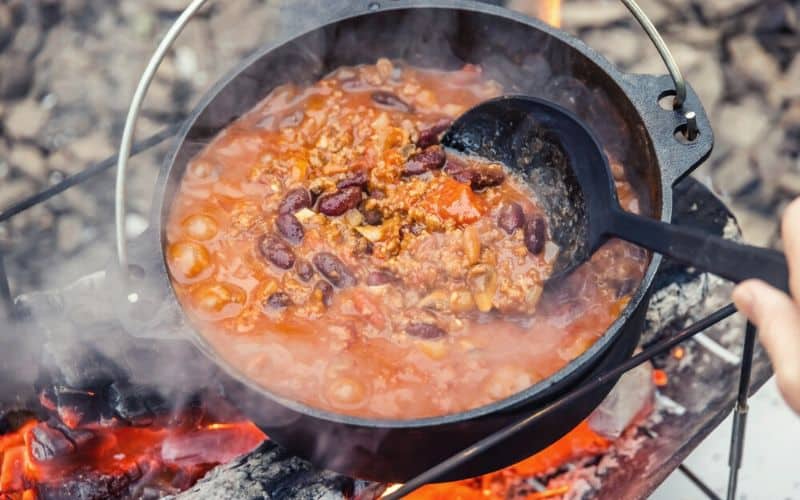 Person stirring pot of chili over a fire