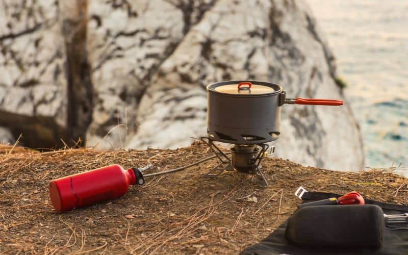 Pot with lid sitting on top a camping stove with fuel line on a clifftop 